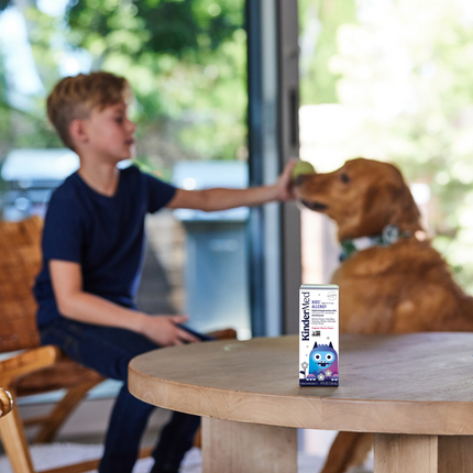 Lifestyle image of Kids allergy product packaging sitting on a kitchen table and a kid is playing with his dog in the background.